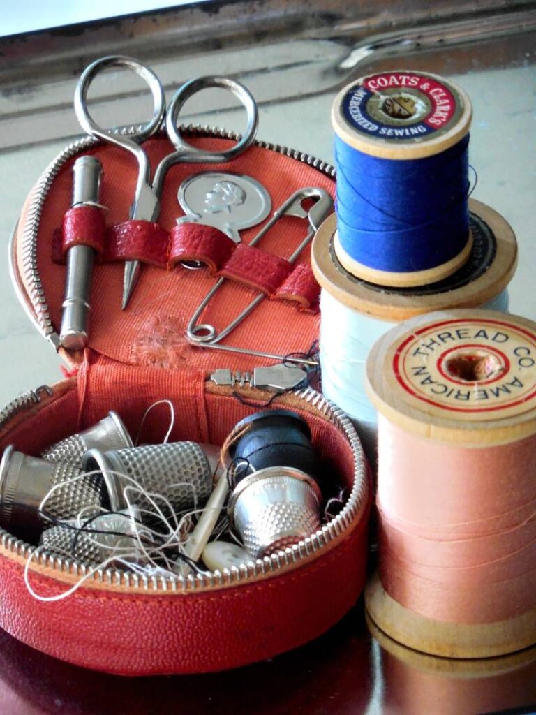 Hilos, dedales, tijeras y otros objetos de costura encima de una mesa.